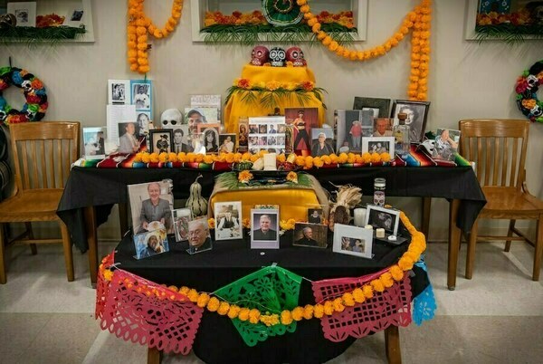 2024 Ofrenda in ILS Lounge decorated with orange marigold garlands, sugar skulls, candles, and framed photos of deceased loved ones.