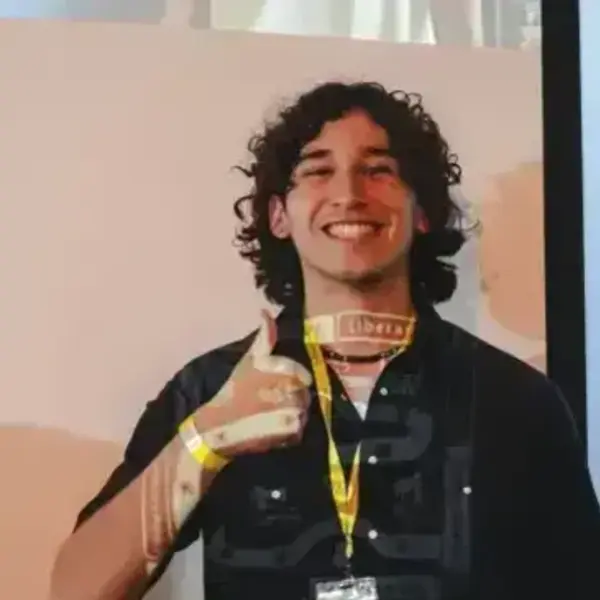 Smiling young man with curly dark hair gives a thumbs up. A projector casts text onto his dark shirt and arm.